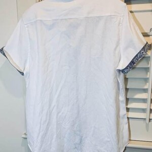 May include: White short-sleeved shirt with a classic collar. The cuffs feature a blue and white patterned design. The shirt is made of a lightweight fabric, suitable for warm weather.