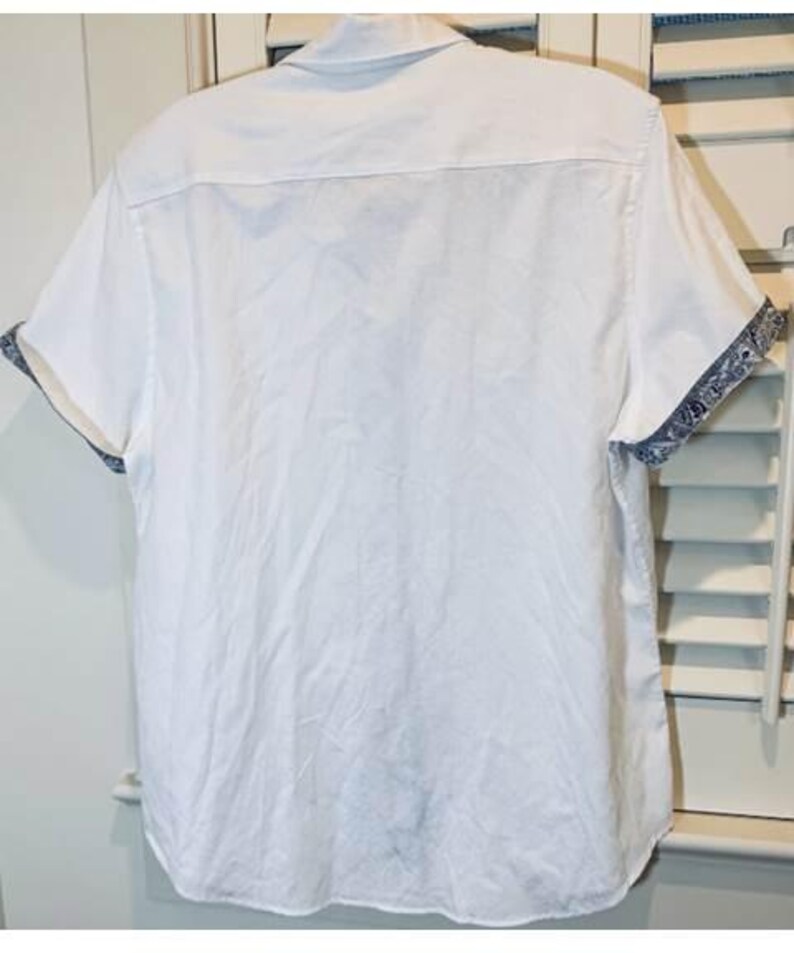 May include: White short-sleeved shirt with a classic collar. The cuffs feature a blue and white patterned design. The shirt is made of a lightweight fabric, suitable for warm weather.