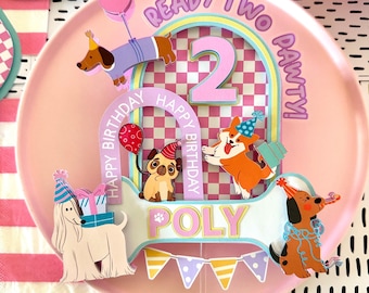 Könnte beinhalten: Rosa Tortenaufsatz mit den Worten "Ready Two Party!" und "Happy Birthday Poly". Das Design zeigt Cartoon-Hunde, die Zahl 2 und ein Schachbrettmuster. Ein rosa Ballon ist ebenfalls abgebildet.