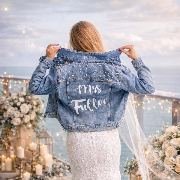 May include: A blue denim jacket featuring white pearl embellishments on the upper back and shoulders. The text "Mrs. Fuller" is printed in white script on the back, with the date "05.12.21" printed in white on the collar.