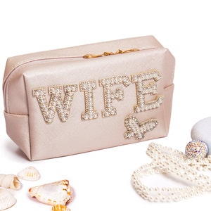 May include: A light pink zippered pouch with the word "WIFE" spelled out in pearl-like beads. The pouch has a gold zipper and a small pearl-like butterfly design.