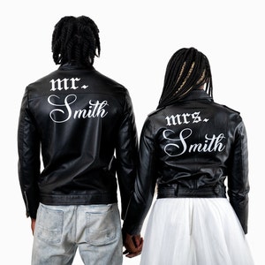 K&ouml;nnte beinhalten: Ein Paar tr&auml;gt schwarze Lederjacken mit wei&szlig;em Text auf dem R&uuml;cken. Die Jacke des Mannes sagt "mr. Smith" und die Jacke der Frau sagt "mrs. Smith".