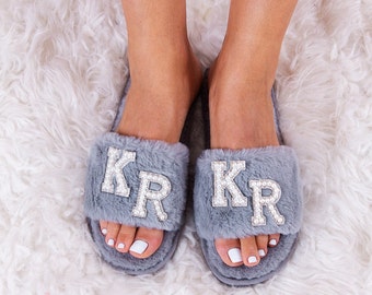 May include: A pair of gray fuzzy slippers with the letters "KR" in rhinestones on each slipper.