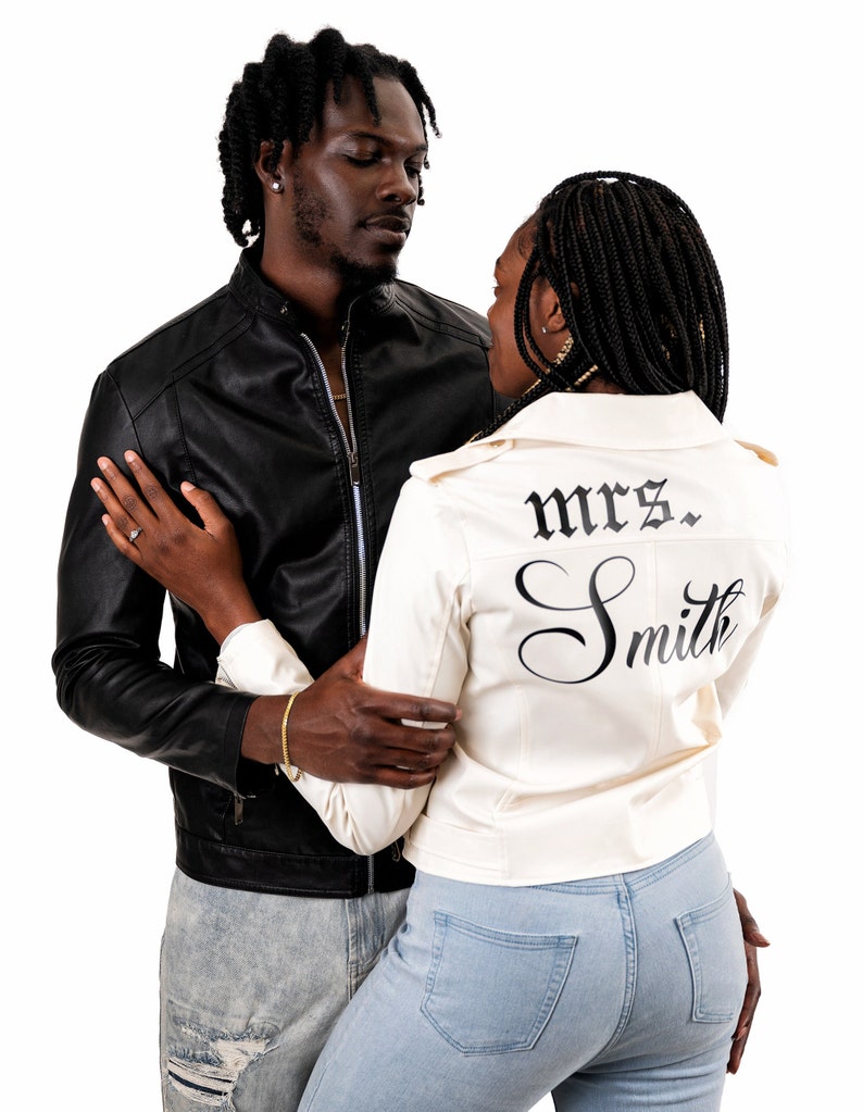 K&ouml;nnte beinhalten: Ein Paar posiert f&uuml;r ein Foto. Die Frau tr&auml;gt eine wei&szlig;e Lederjacke mit dem Text "mrs. Smith" auf dem R&uuml;cken. Der Mann tr&auml;gt eine schwarze Lederjacke.