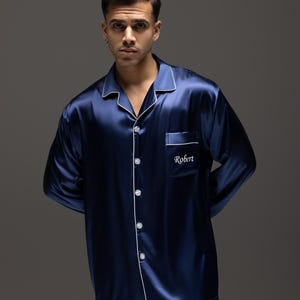 May include: A navy blue satin pajama top with white piping and a white embroidered pocket that says "Robert".