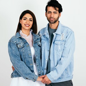 K&ouml;nnte beinhalten: Ein Paar tr&auml;gt blaue Jeansjacken, die Jacke der Frau ist mit Perlen verziert, sie stehen eng beieinander und l&auml;cheln in die Kamera.