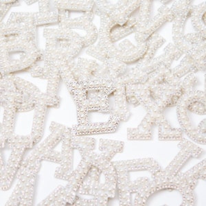 May include: A close-up of a pile of pearl-covered letters, with the letter "E" in the center.