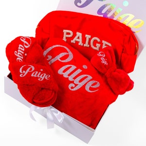 May include: A red gift box filled with a red robe, slippers, and a makeup bag, all personalized with the name "Paige" in silver glitter.