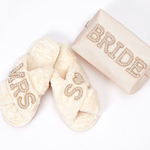May include: A pair of white faux fur slippers with the word "MRS" and a heart on one slipper and the word "MISS" on the other slipper. A white clutch with the word "BRIDE" in gold rhinestones is also included.