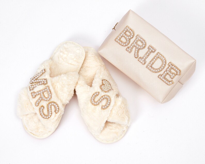 May include: A pair of white faux fur slippers with the word "MRS" and a heart on one slipper and the word "MISS" on the other slipper. A white clutch with the word "BRIDE" in gold rhinestones is also included.