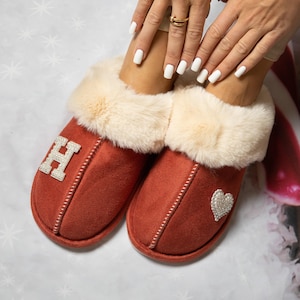Pu&ograve; includere: Un paio di pantofole color ruggine con una fodera in pelliccia sintetica color crema. La pantofola sinistra &egrave; decorata con una grande lettera H impreziosita da perle bianche, mentre la destra presenta una toppa a forma di cuore di perle.