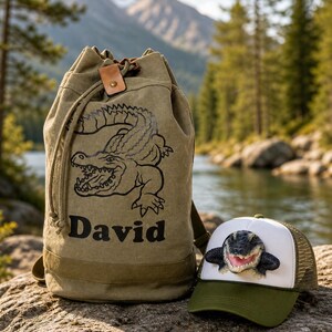 May include: An olive green backpack with a drawstring closure and a leather accent, featuring a black and grey alligator design and the name "David." Beside it is a green and white trucker hat with an alligator figure.