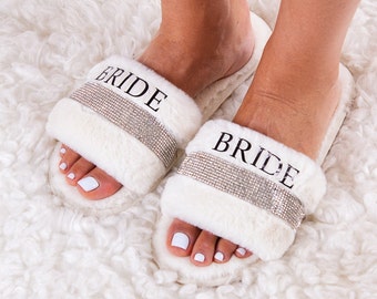 May include: White faux fur slippers with a rhinestone trim and the word "BRIDE" printed on the front.