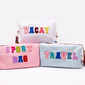 Puede incluir: Tres bolsas de lona coloridas con diferentes palabras bordadas. La bolsa de arriba es blanca con la palabra "VACAY" en letras arco&iacute;ris. La bolsa del medio es rosa con las palabras "SPORT BAG" en letras arco&iacute;ris. La bolsa de abajo es azul claro con la palabra "TRAVEL" en letras arco&iacute;ris.