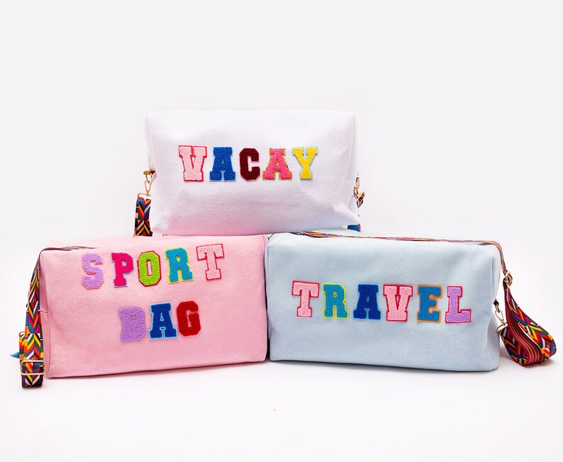 Puede incluir: Tres bolsas de lona coloridas con diferentes palabras bordadas. La bolsa de arriba es blanca con la palabra "VACAY" en letras arco&iacute;ris. La bolsa del medio es rosa con las palabras "SPORT BAG" en letras arco&iacute;ris. La bolsa de abajo es azul claro con la palabra "TRAVEL" en letras arco&iacute;ris.
