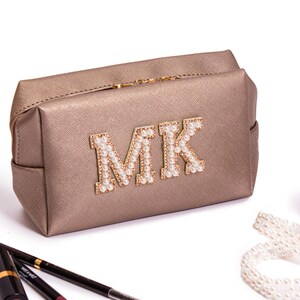 May include: A gold-colored makeup bag with a zipper closure. The bag has the letters "MK" on the front, made of white pearls.