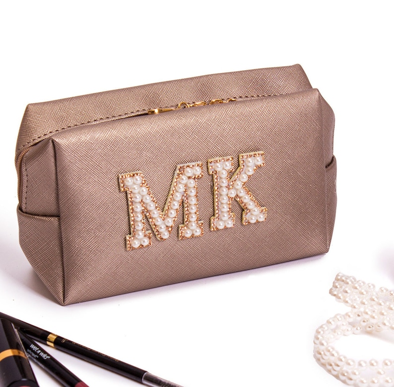 May include: A gold-colored makeup bag with a zipper closure. The bag has the letters "MK" on the front, made of white pearls.