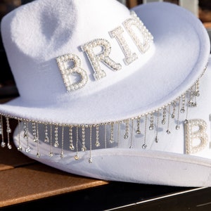 May include: White cowboy hat with a beaded "Bride" embellishment and a fringe trim.
