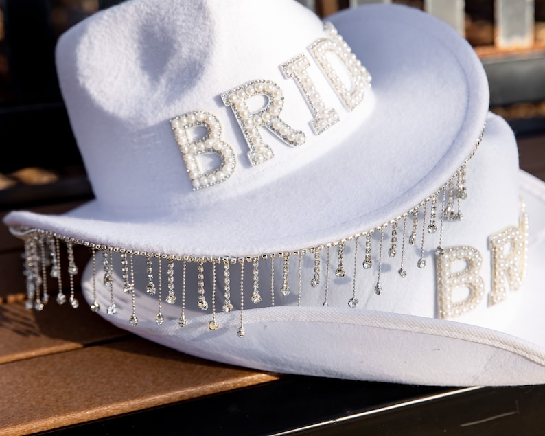 May include: White cowboy hat with a beaded "Bride" embellishment and a fringe trim.
