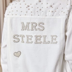 May include: White denim jacket with pearl embellishments and the text "MRS STEELE" in rhinestones. A small pearl heart is below the text.