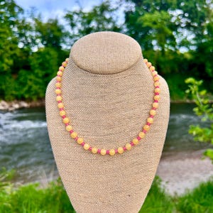 May include: A beaded necklace featuring a repeating pattern of round, translucent yellow beads and smaller, vibrant pink beads. The necklace is arranged in a circular shape, showcasing a consistent alternating sequence of these two distinct bead colors.