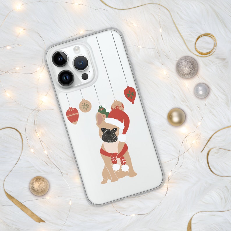 Puede incluir: Una funda transparente para tel&eacute;fono con fondo blanco y una imagen de dibujos animados de un bulldog franc&eacute;s con un gorro de Pap&aacute; Noel y una bufanda. El bulldog est&aacute; rodeado de adornos navide&ntilde;os.