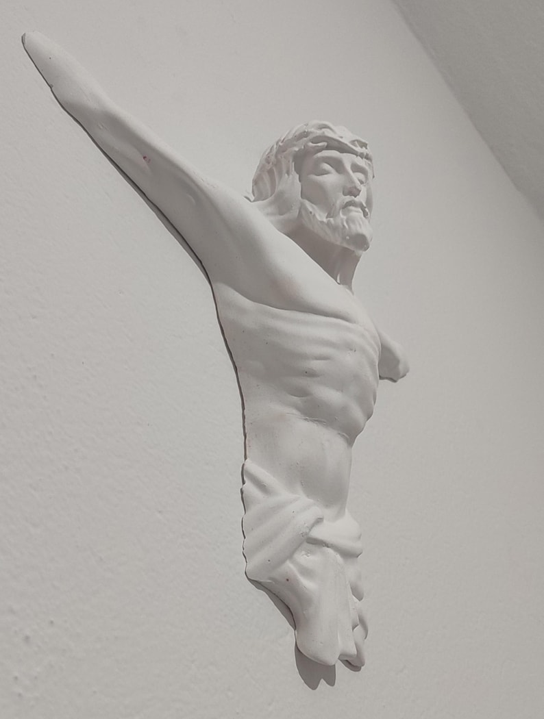 May include: A white plaster sculpture of Jesus Christ on a wall. The sculpture shows Jesus with a crown of thorns, a beard, and outstretched arms. The figure is draped with a cloth around the waist.