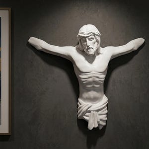 May include: A white sculpture of a figure with outstretched arms, wearing a crown of thorns and a draped cloth. The sculpture is mounted on a dark grey wall. A framed abstract painting is visible on the left.