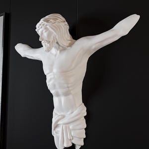 May include: A white sculpture of a man with outstretched arms, a beard, and a crown of thorns, mounted on a black wall. The figure is draped with fabric around the lower body. The sculpture is a religious depiction.