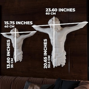 May include: Two white wall sculptures of a figure with outstretched arms, one measuring 40 cm wide and 35 cm tall, the other 60 cm wide and 52.5 cm tall. The sculptures are mounted on a dark brown wall. Measurements are provided in inches and cm.