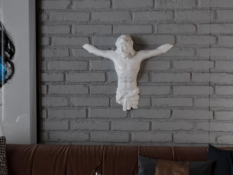 May include: A white sculpture of Jesus Christ on a cross, mounted on a grey brick wall. The sculpture depicts Jesus with outstretched arms and a crown of thorns. The wall is made of grey bricks.