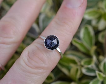 Puede incluir: Un anillo de plata con una piedra redonda de color azul oscuro engastada en un engaste de bisel.
