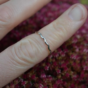 May include: A silver ring with a wavy design, worn on a finger.