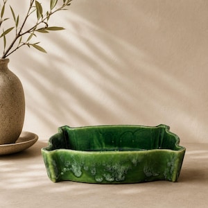 May include: A rectangular ceramic dish with a vibrant emerald green glaze featuring a glossy finish and subtle variations in color intensity. The dish has slightly raised, curved edges and a smooth, reflective surface throughout its interior.