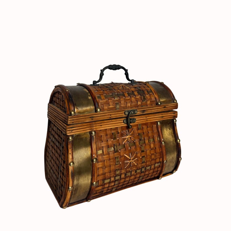 May include: A decorative, woven bamboo chest with brass accents. The chest features a curved top, a black handle, and a latch closure. The sides are reinforced with brass and secured with small rivets. The woven pattern is a mix of light and dark brown.