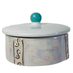 May include: A white ceramic trinket box with a teal knob on the lid. The box has a pearlescent finish and gold accents.