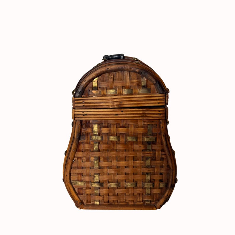 May include: A vintage, woven basket-style box with a curved top and a latch closure. The box is made of light brown woven material with accents of gold-colored metal and dark brown trim. The box has a unique shape and design.