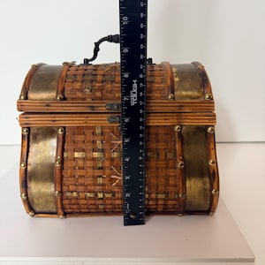 May include: A decorative woven chest with brass accents and a black handle. The chest is approximately 10 inches tall. The chest has a rectangular shape with rounded edges and is secured with a metal clasp.