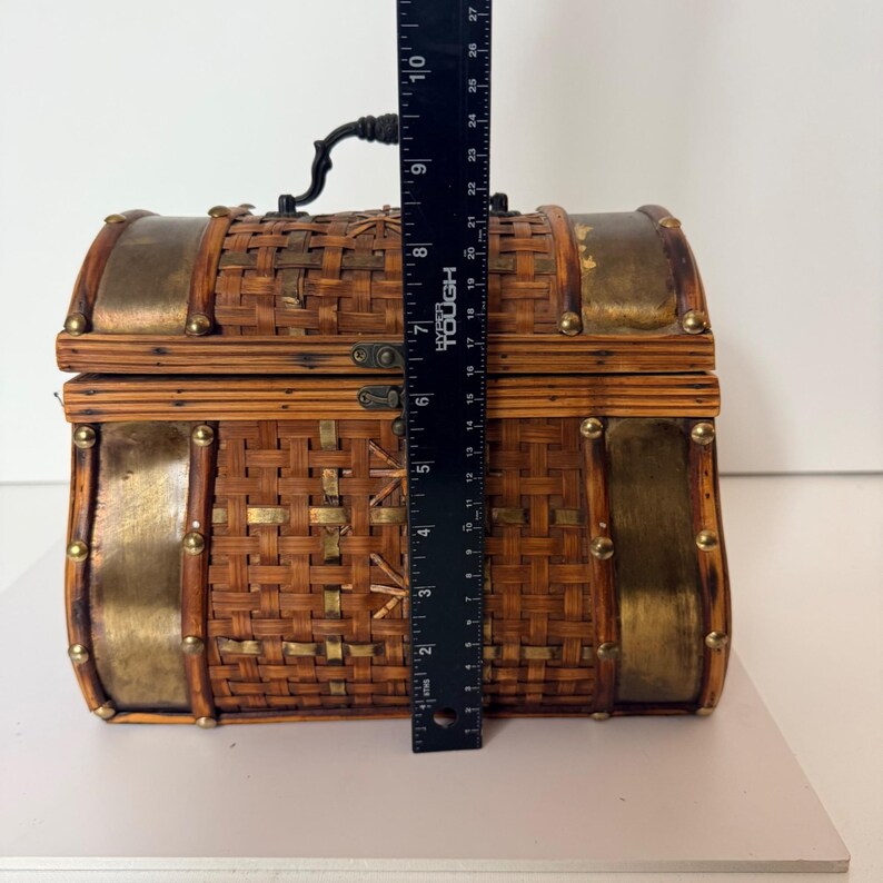 May include: A decorative woven chest with brass accents and a black handle. The chest is approximately 10 inches tall. The chest has a rectangular shape with rounded edges and is secured with a metal clasp.