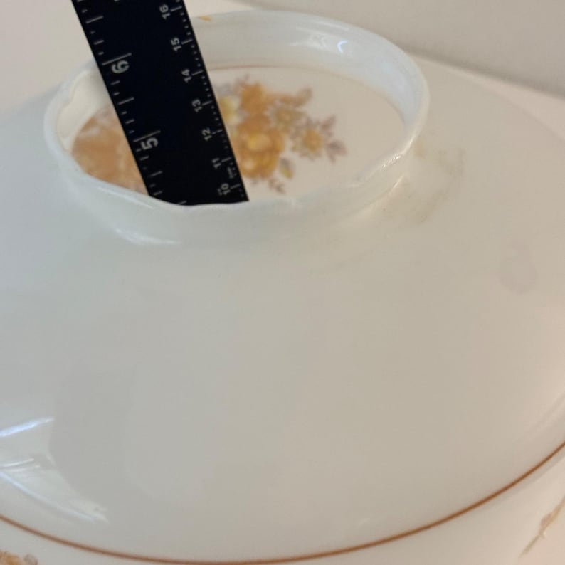 May include: A white, vintage lampshade with a scalloped edge and a floral design. The lampshade has a diameter of approximately 12 inches. A black ruler is placed inside the lampshade to measure its depth.