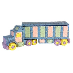 Könnte beinhalten: Ein blauer, rosa und grüner Spielzeug-LKW mit Patchwork-Design. Der LKW hat einen Pritschenwagen und Räder mit gelben Blumen.