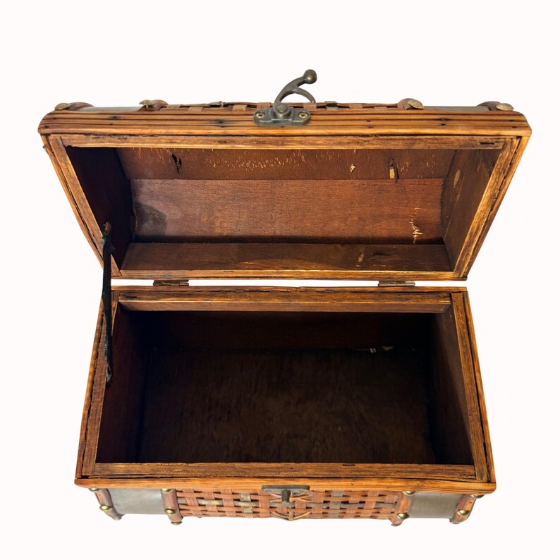 May include: Open wooden chest with a hinged lid and a metal clasp. The chest is made of woven and solid wood, with metal accents. The interior is dark, and the chest appears to be empty. The chest is designed to store items.