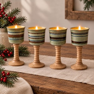 May include: Four ceramic candle holders with light green, blue, and brown horizontal stripes. Each holder features a ribbed, light-colored wooden pedestal base and contains a lit tea light candle, creating a warm glow from within the cup.