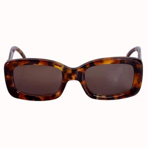 Puede incluir: Gafas de sol con estampado de carey y lentes rectangulares. Las monturas presentan un diseño clásico de carey en tonos marrones y ámbar. Las lentes son de color marrón liso, contrastando con las monturas estampadas. Estilo retro y vintage.