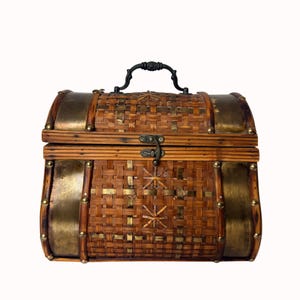 May include: A woven brown chest with brass accents and a black handle. The chest features a woven pattern with brass studs and decorative brass plates on the sides. The chest has a metal clasp closure.