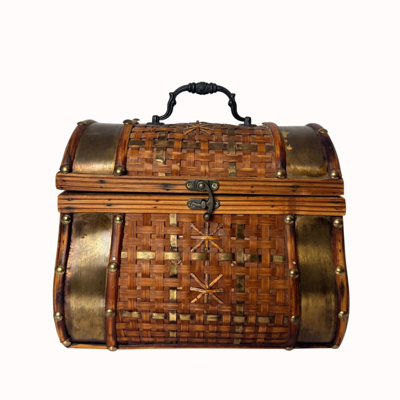 May include: A woven brown chest with brass accents and a black handle. The chest features a woven pattern with brass studs and decorative brass plates on the sides. The chest has a metal clasp closure.
