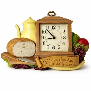 Op de afbeelding: Een decoratieve houten klok met een vierkante wijzerplaat, met een brood, een theepot en fruit. De klok geeft ongeveer 8:55 uur aan. Een banner luidt "Give us this day our daily bread..."