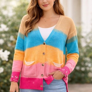 May include: A colorful cardigan with a V-neck and button closure. The sweater features a gradient design with shades of tan, blue, orange, pink, and fuchsia. It has two front pockets and decorative cuffs. The cardigan is made of a soft, knitted material.