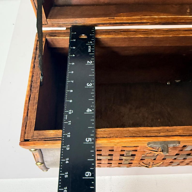 May include: A wooden chest with a woven front and a hinged lid. The chest is brown with a dark interior. A ruler shows the chest is approximately 6 inches deep. The chest has a metal clasp and decorative accents.