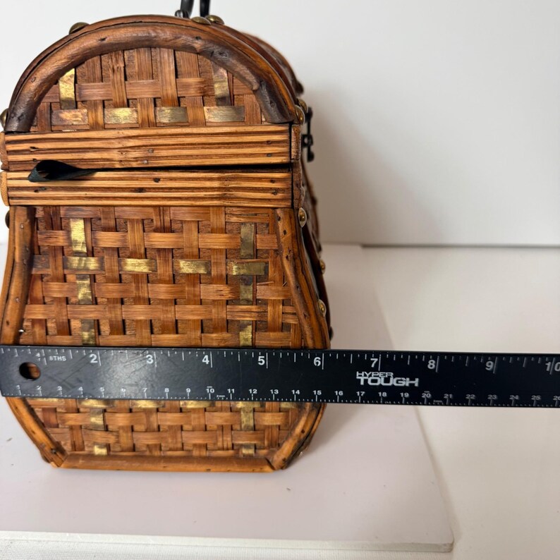 May include: A vintage woven basket purse with a curved top and a handle. The purse is made of brown woven material with gold-colored metal accents. The purse is approximately 6 inches wide.